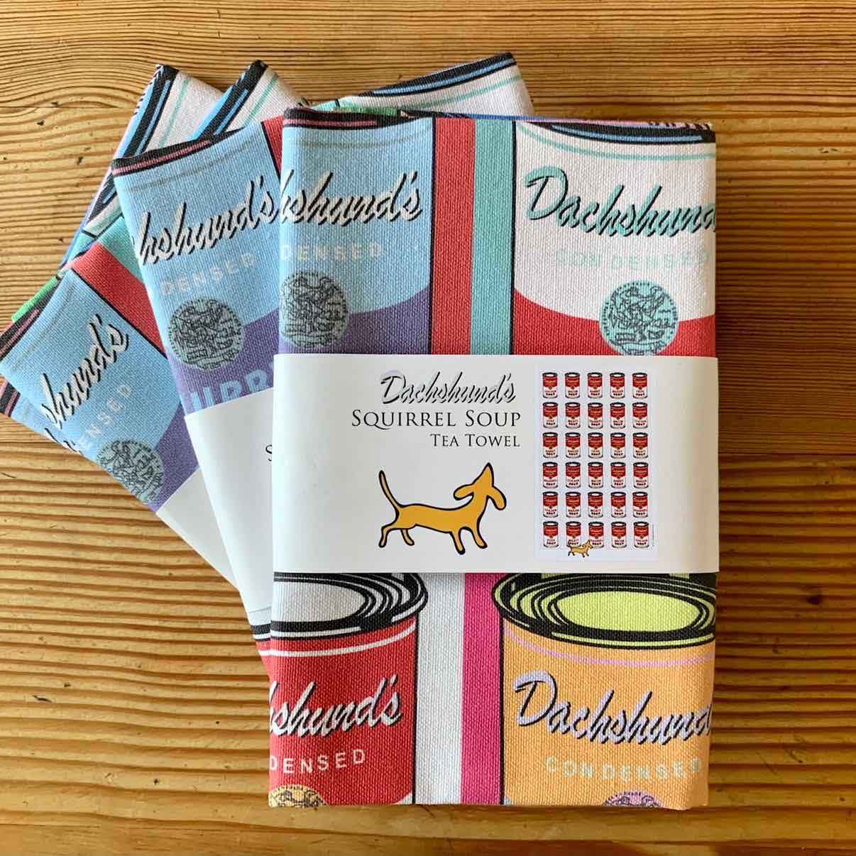 A folded set of Dachshund Squirrel Soup Tea Towels. The design is based on Warhols Campbells Soup Tins and given a clever Dachshund theme.