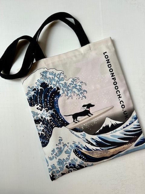 Humorous design Tote bag with the image of the Hokusai Wave plus a small dachshund on a surfboard. Black handle straps.